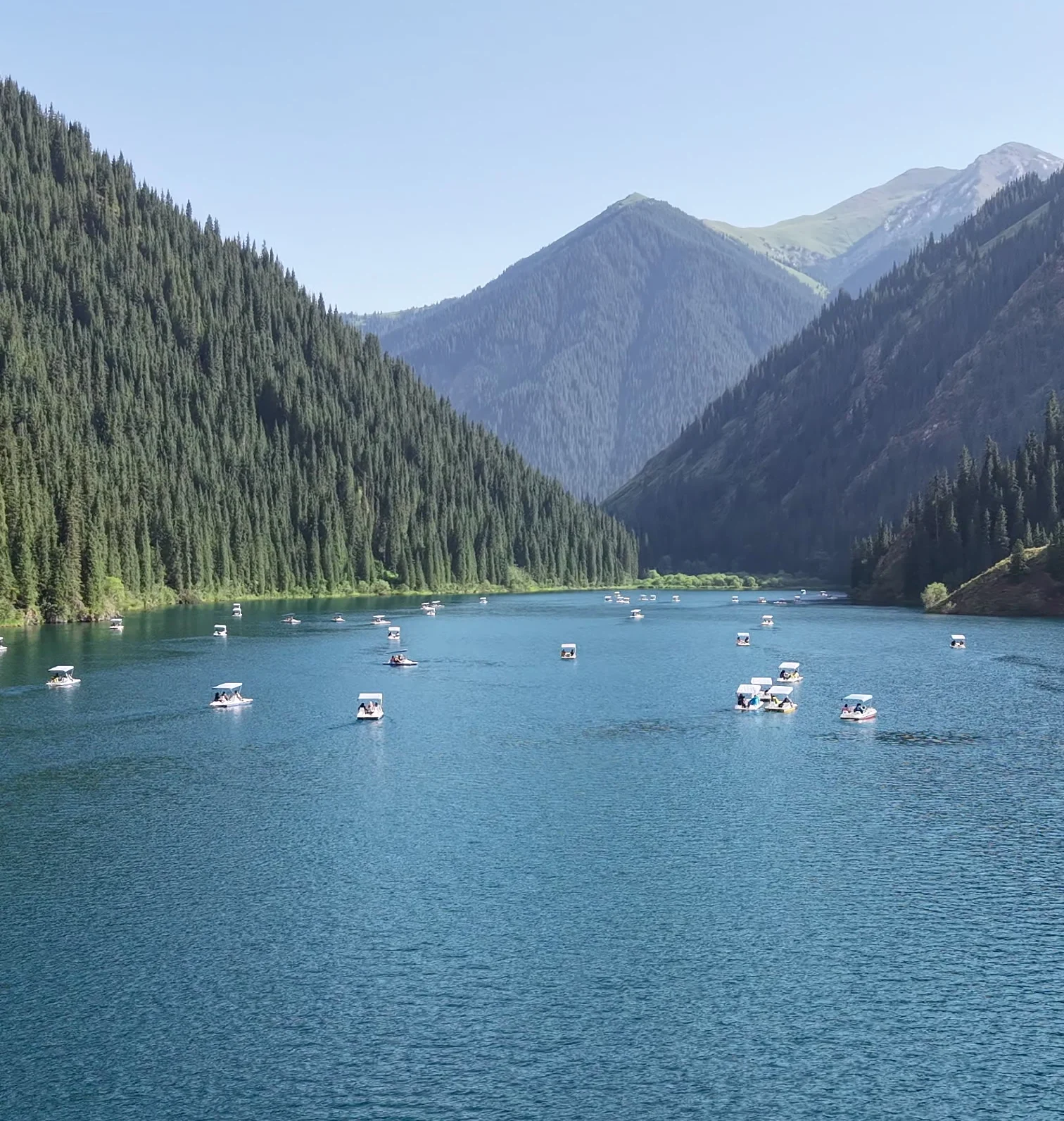 Kolsay Lake from above: boats on the water between forested slopes