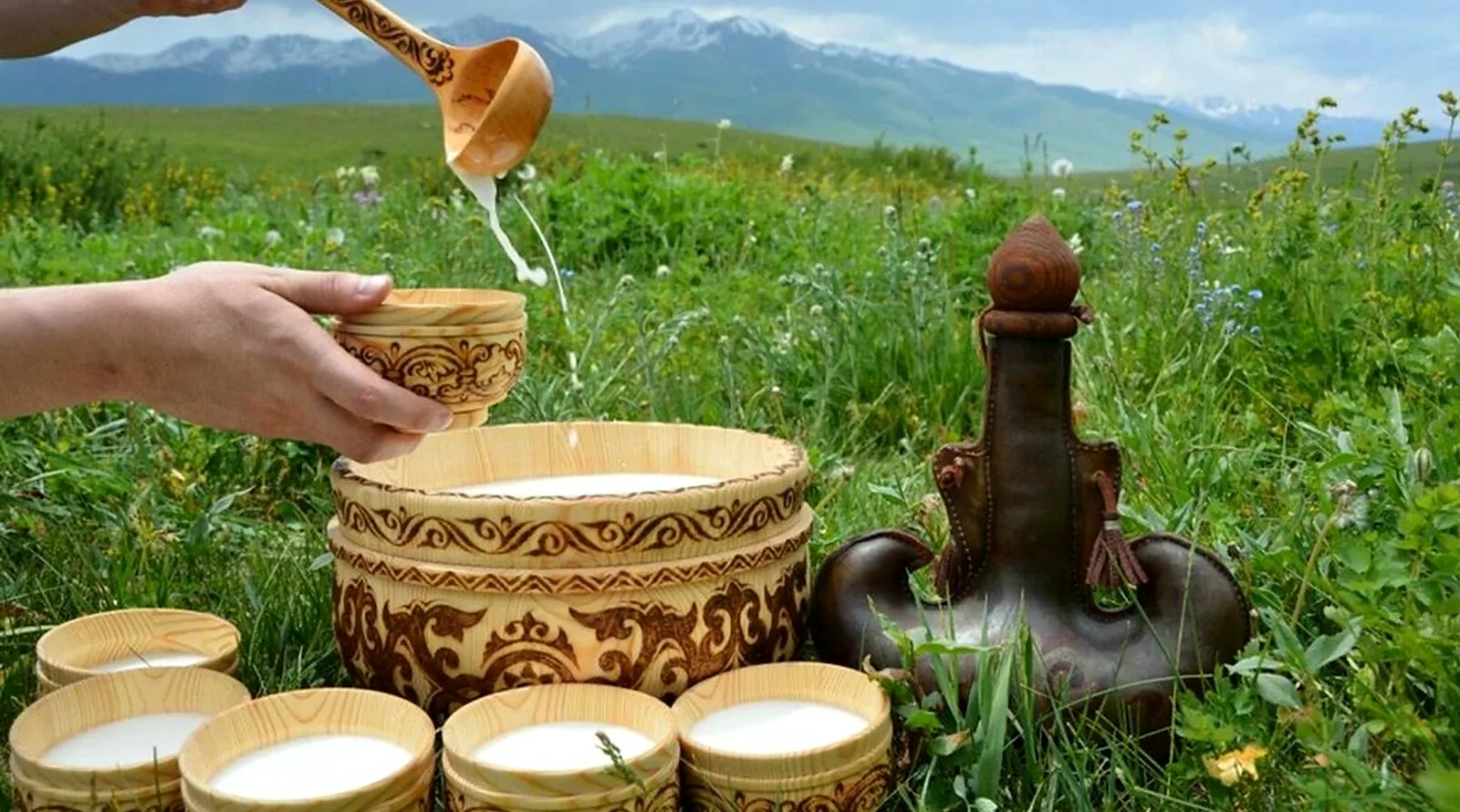 Mare’s milk poured from a wooden ladle into carved bowls in a mountain meadow