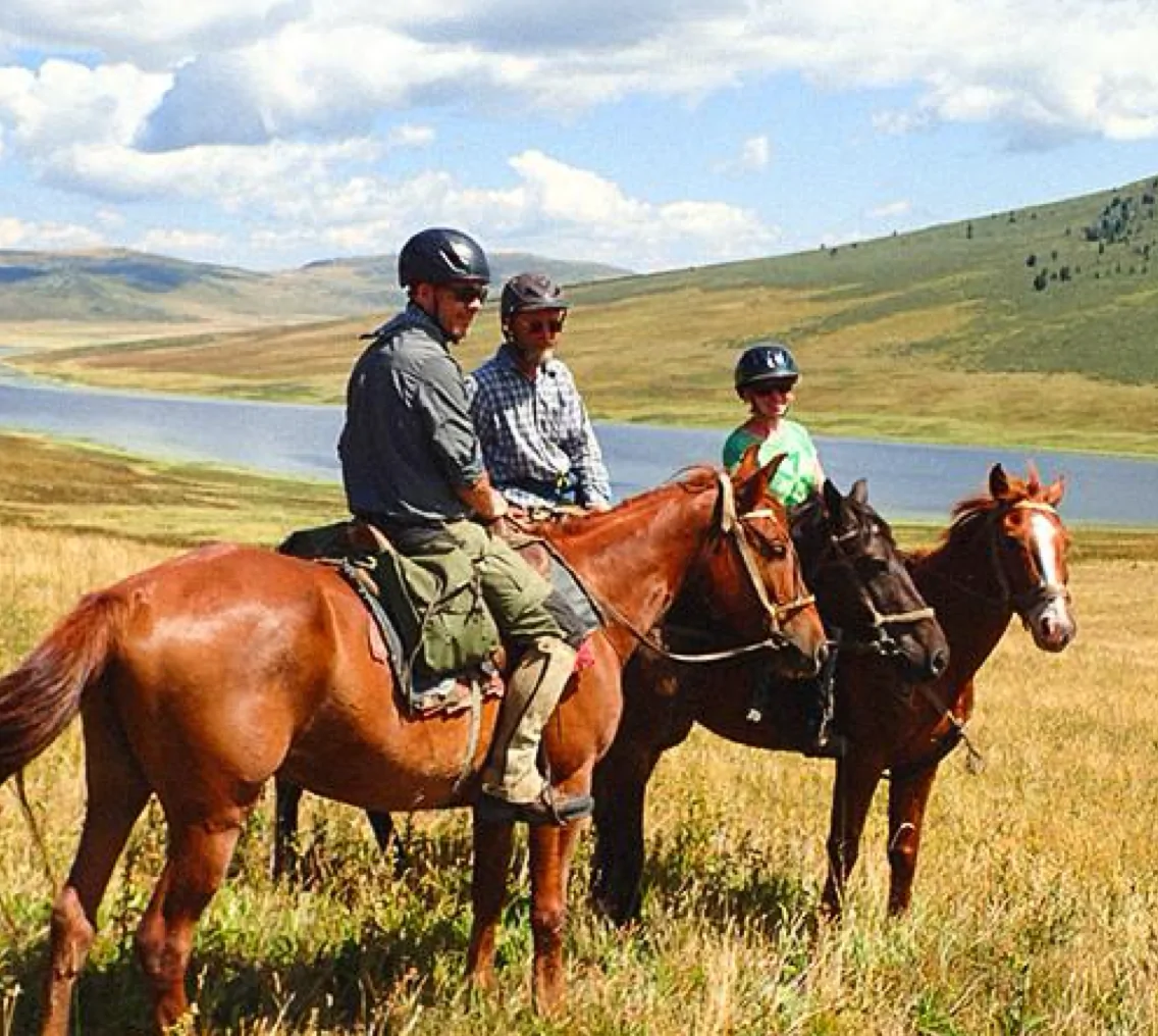 Three riders on horseback in the open steppe beside a lake