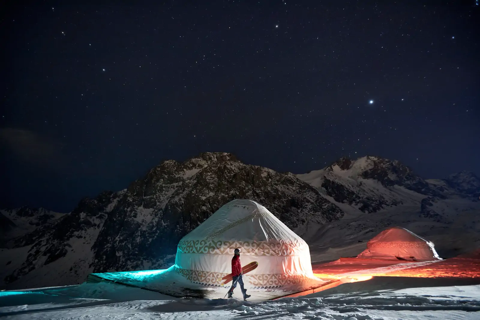 A lit yurt under a starry sky in the mountains