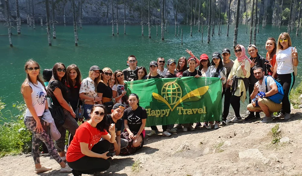The Happy Travel team with a company flag on the shore of Lake Kaindy